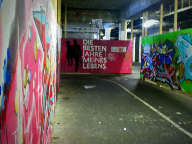Graffito an einem Bauzaun in einer heruntergekommenen, dreckigen, vermüllten und apokalyptisch wirkenden Tiefgarage im Ihmezentrum zu Hannover. Zwei Umrisse von einkaufenden Menschen, dazu der Text 'Die besten Jahre meines Lebens'
